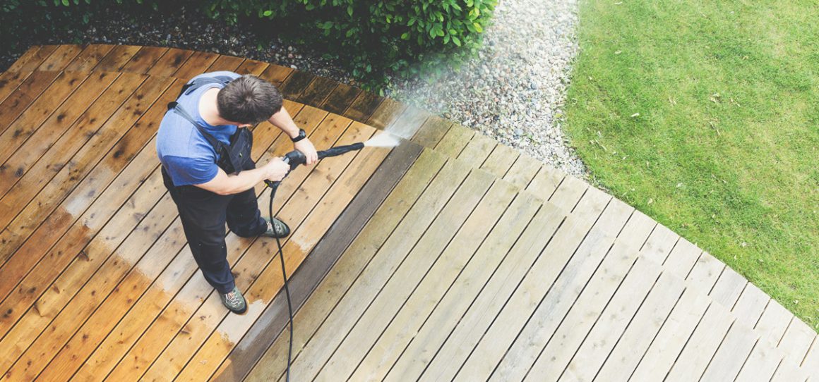 Een man maakt zijn houten terras schoon met behulp van een hogedrukreiniger