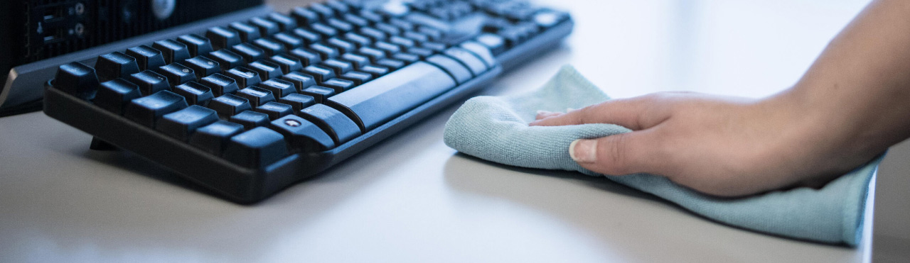 De hand van een schoonmaker die een bureau schoon maakt met behulp van een microvezeldoek